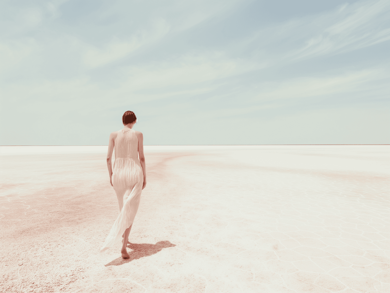 A woman in a white dress walking across a pale salt flat